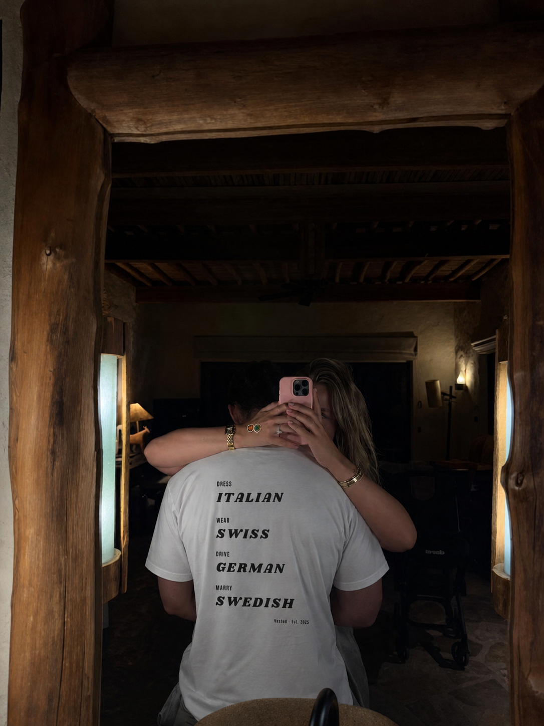 Person wearing a white t-shirt with text in a dimly lit room.